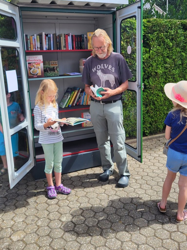 Kinder und Erwachsene weihen den Bücherschrank ein und suchen sich Bücher aus.