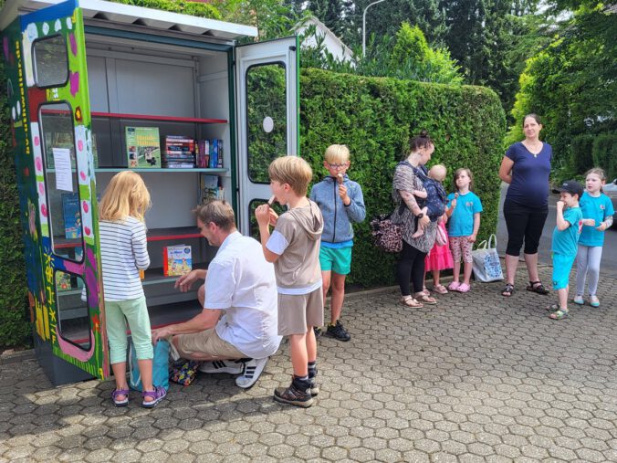 Personen stehen vor dem Bücherschrank bei der Eröffnung und räumen Bücher ein.