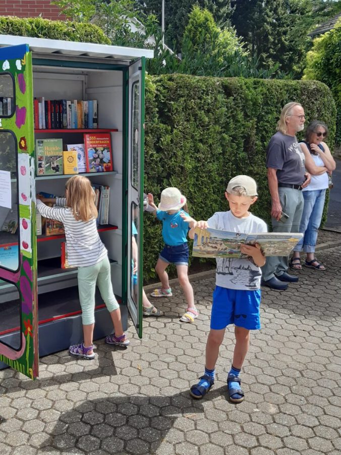 Kinder und Erwachsene weihen den Bücherschrank ein und suchen sich Bücher aus.